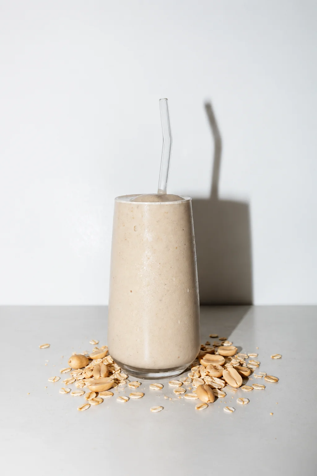 Peanut Oat smoothie in a glass with a straw, with oats scattered beside it